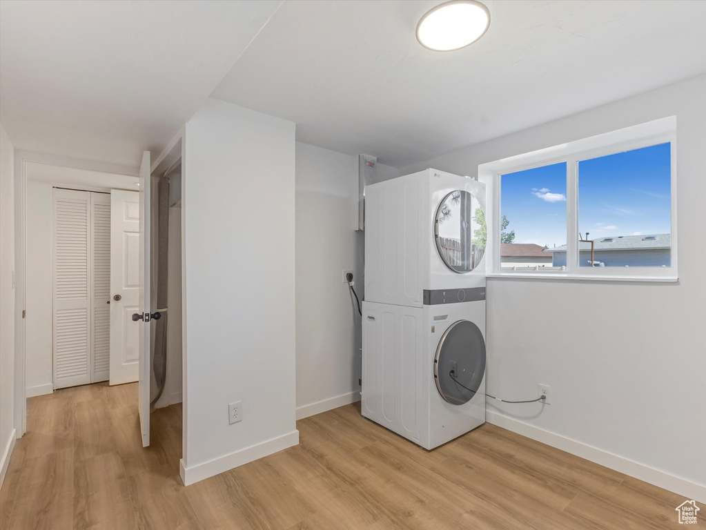Laundry area with stacked washing machine and dryer and light wood-type flooring
