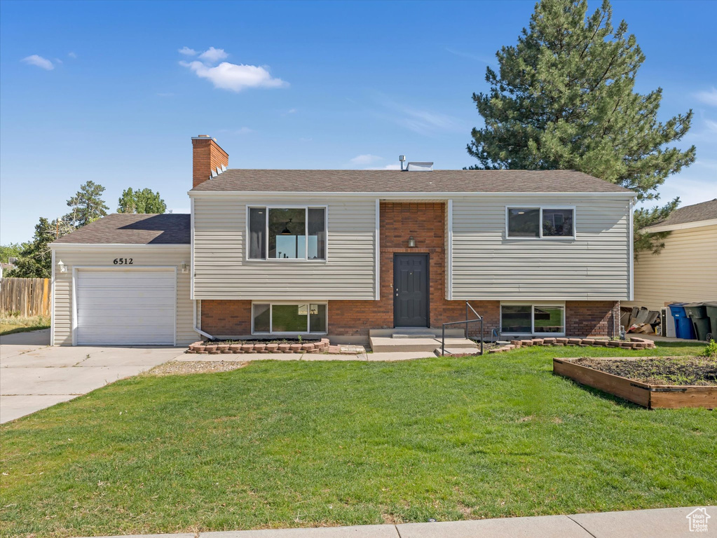 Raised ranch featuring a garage, concrete driveway, a chimney, and brick siding