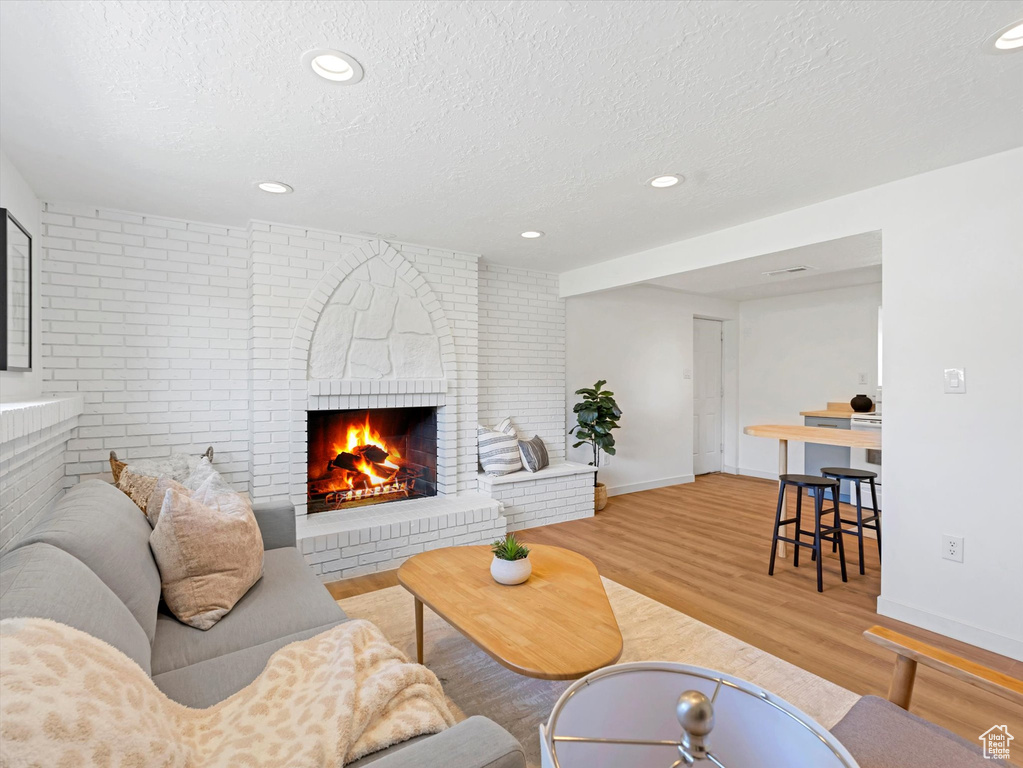 Living room with a textured ceiling, light wood-type flooring, a brick fireplace, recessed lighting, and brick wall