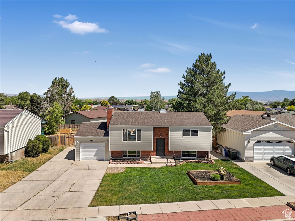 Split foyer home with concrete driveway, brick siding, a garage, and a residential view