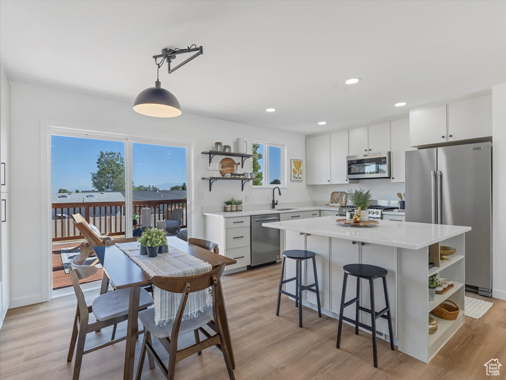 Kitchen with stainless steel appliances, open shelves, light countertops, light wood finished floors, and recessed lighting