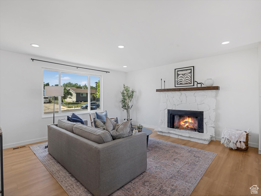 Living room with a stone fireplace, light wood-style floors, and recessed lighting