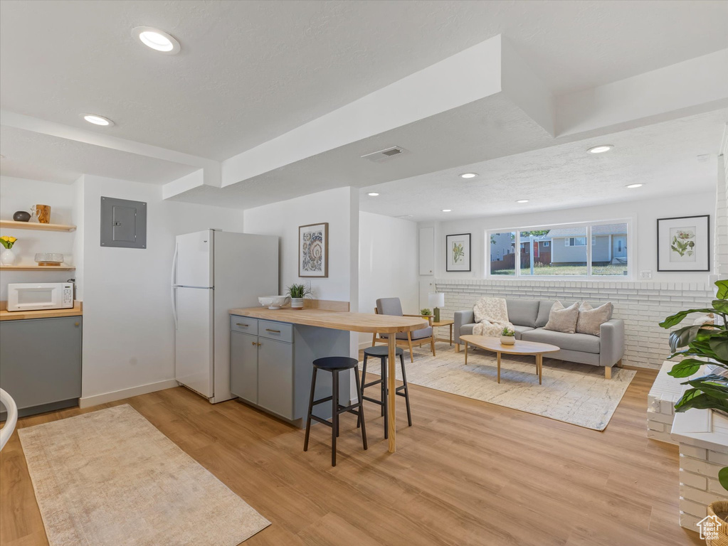 Kitchen with white appliances, electric panel, light wood-style floors, recessed lighting, and a breakfast bar