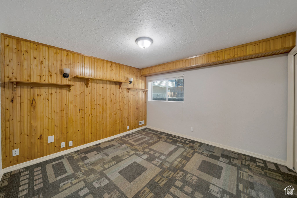 Spare room featuring a textured ceiling, wood walls, and dark colored carpet