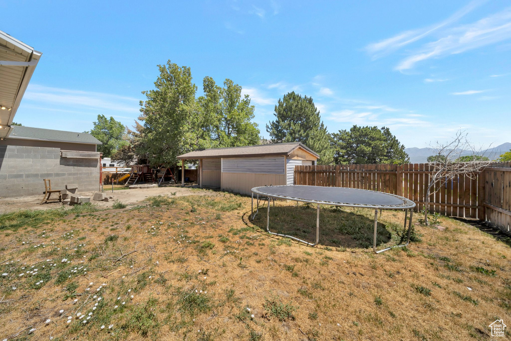 Fenced backyard featuring a trampoline and an outbuilding