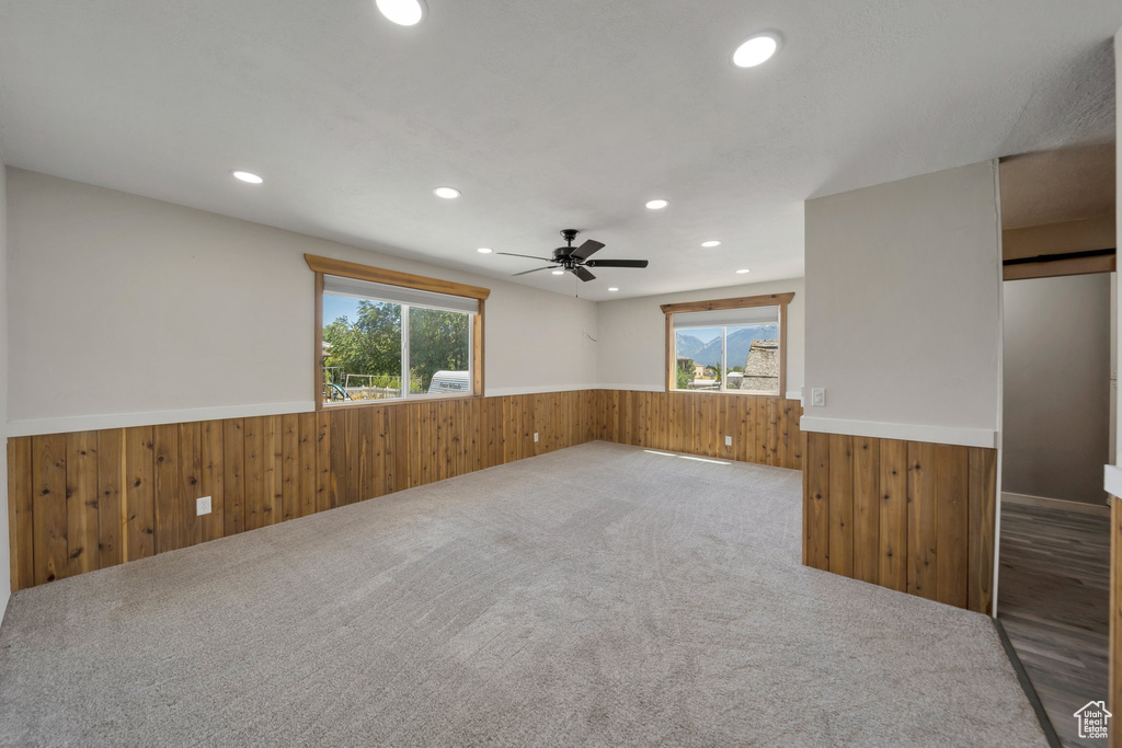 Carpeted spare room with wainscoting, wood walls, healthy amount of natural light, recessed lighting, and a ceiling fan