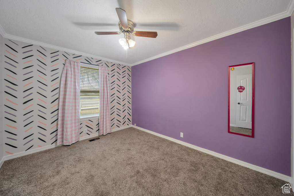 Carpeted empty room featuring ornamental molding, ceiling fan, wallpapered walls, and an accent wall