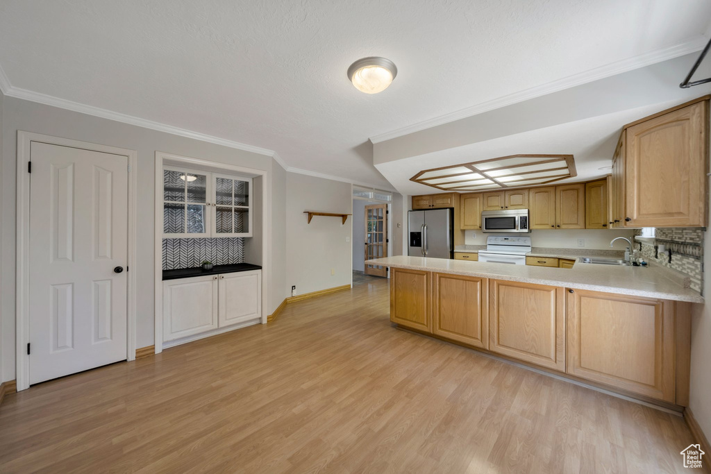 Kitchen with appliances with stainless steel finishes, light wood-type flooring, light countertops, a peninsula, and ornamental molding