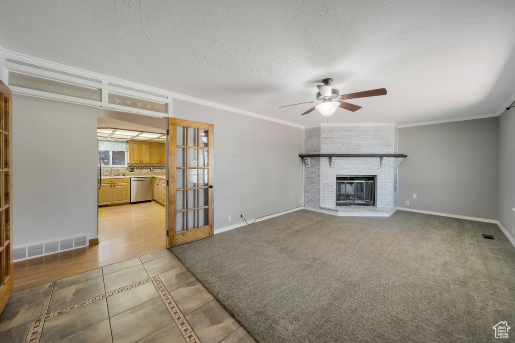 Unfurnished living room with a ceiling fan, light tile patterned flooring, crown molding, a fireplace, and a textured ceiling