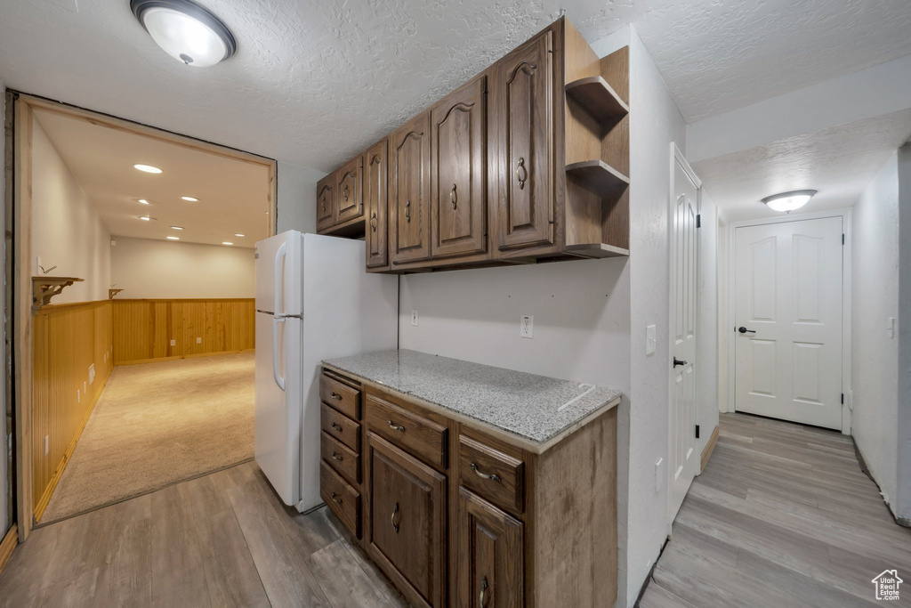 Kitchen with a textured ceiling, open shelves, light wood finished floors, freestanding refrigerator, and a wainscoted wall