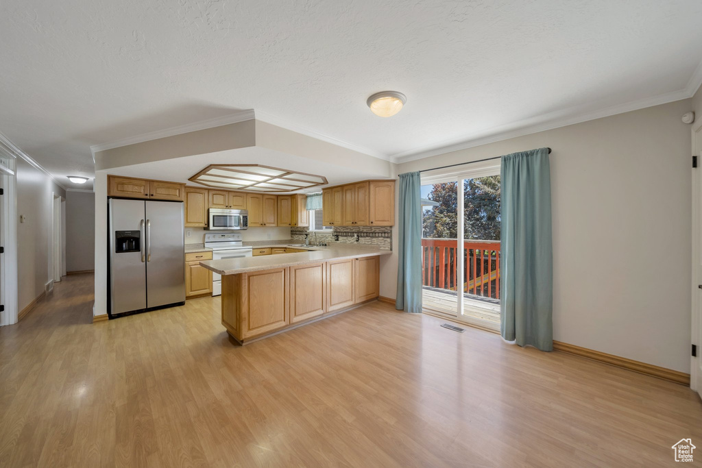 Kitchen featuring appliances with stainless steel finishes, light countertops, light wood-type flooring, ornamental molding, and a peninsula