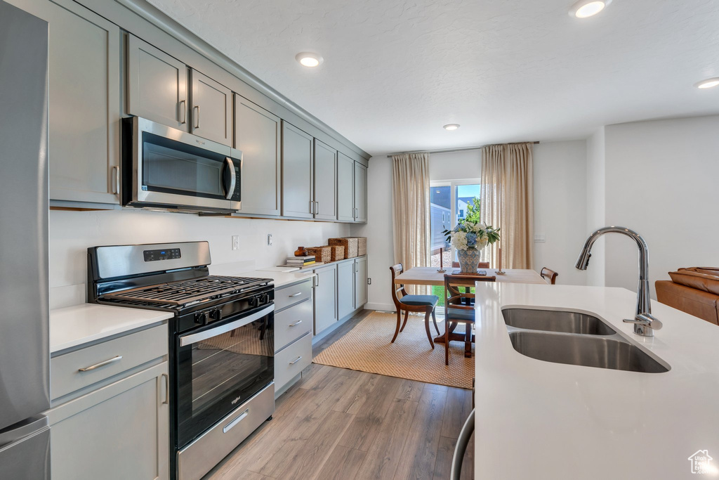 Kitchen with stainless steel appliances, gray cabinetry, light countertops, recessed lighting, and light wood-type flooring