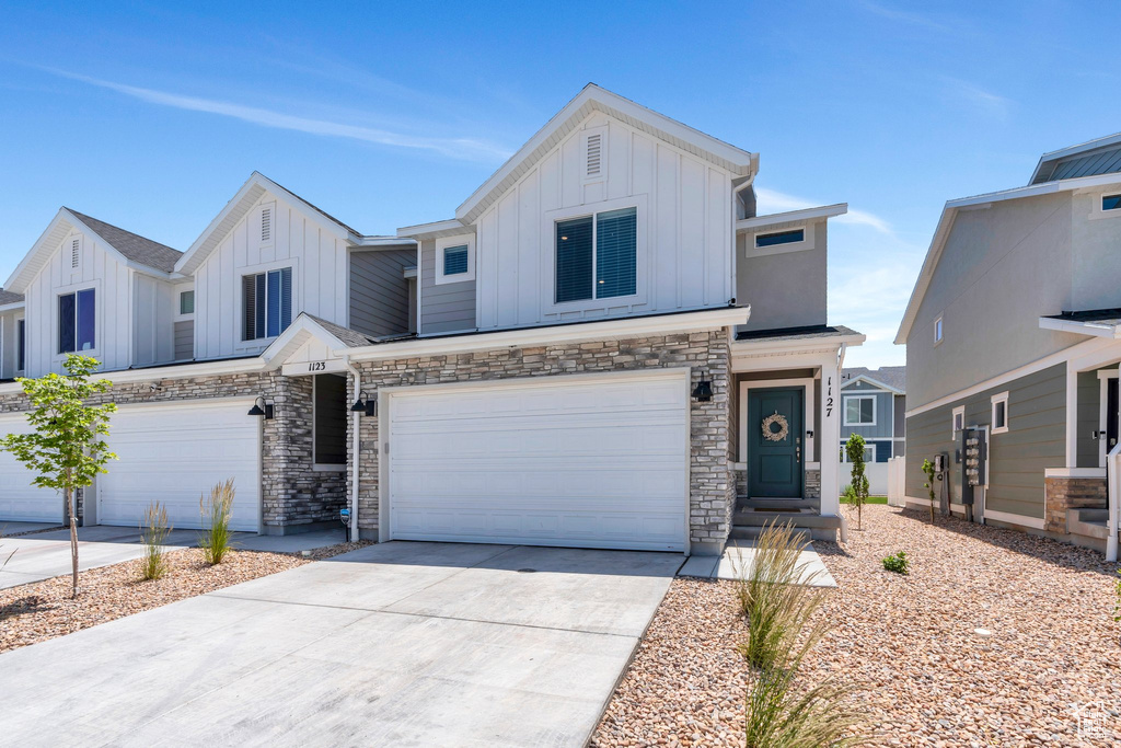 View of front facade featuring board and batten siding, an attached garage, concrete driveway, and stone siding