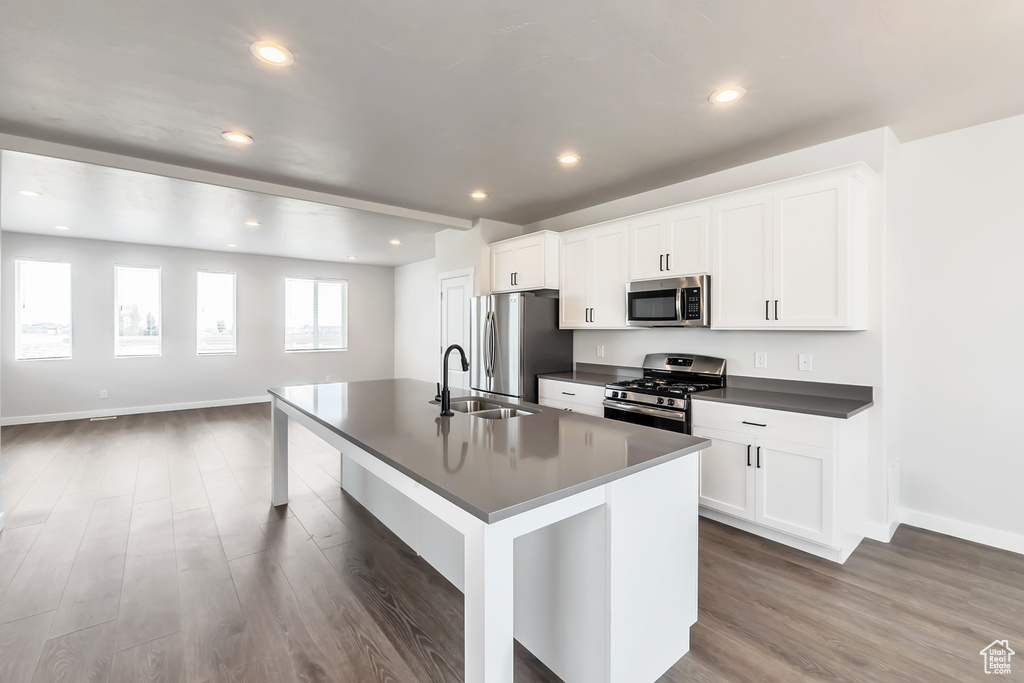 Kitchen featuring stainless steel appliances, dark countertops, wood finished floors, a center island with sink, and baseboards
