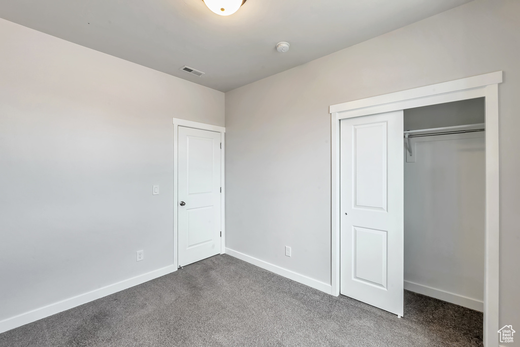 Unfurnished bedroom featuring dark carpet, a closet, and baseboards