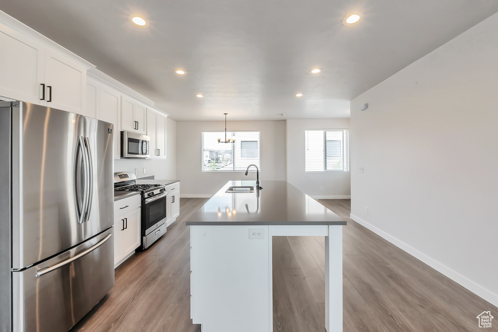 Kitchen with appliances with stainless steel finishes, a sink, a chandelier, a center island with sink, and baseboards