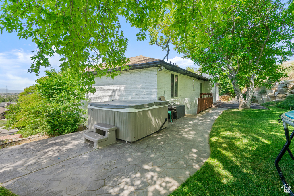 View of property exterior featuring a hot tub, a patio area, brick siding, and a lawn