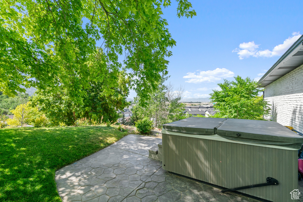 View of green lawn with a hot tub and a patio