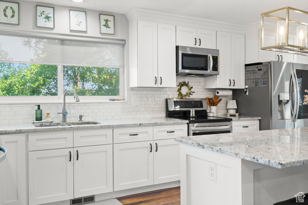 Kitchen with appliances with stainless steel finishes, white cabinetry, decorative backsplash, and light stone countertops