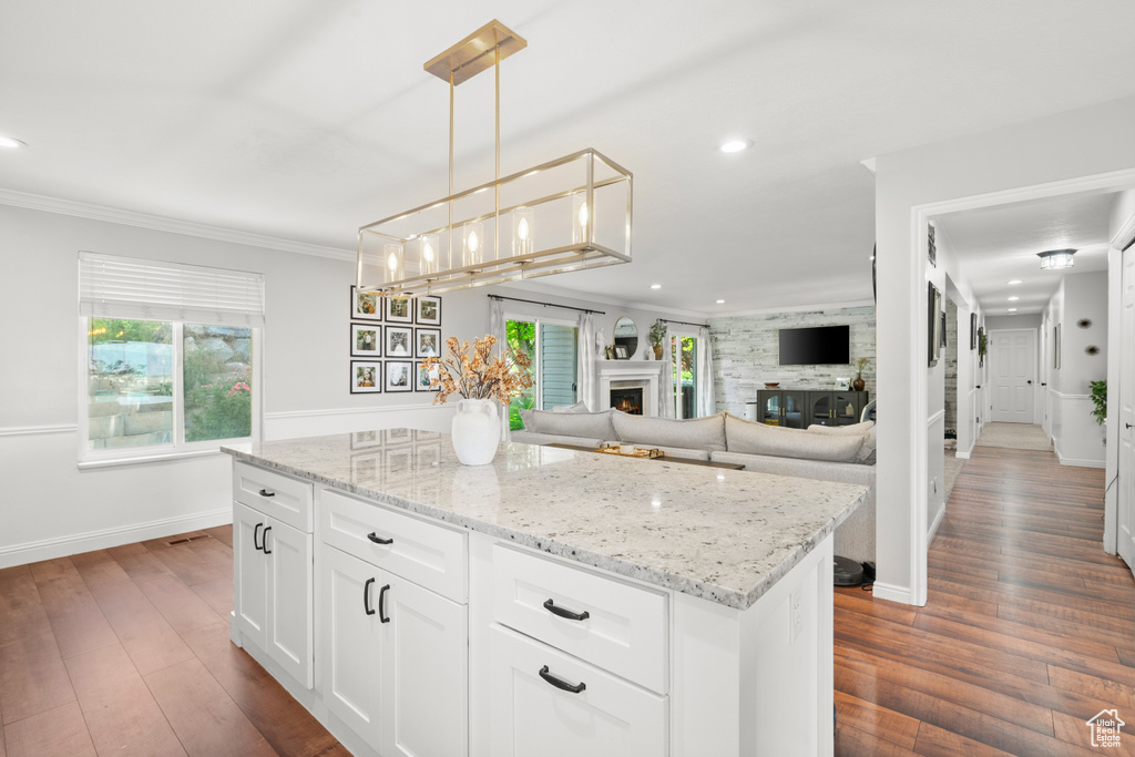 Kitchen featuring plenty of natural light, a warm lit fireplace, light stone countertops, recessed lighting, and ornamental molding