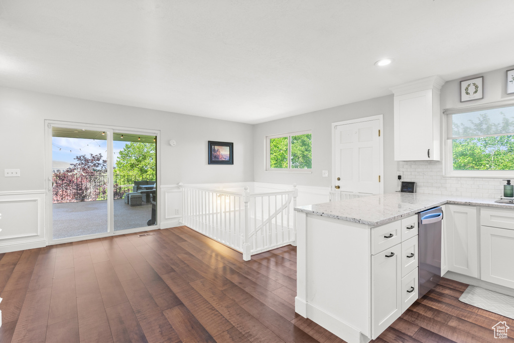 Kitchen with a peninsula, dishwasher, dark wood-style flooring, white cabinets, and light stone counters