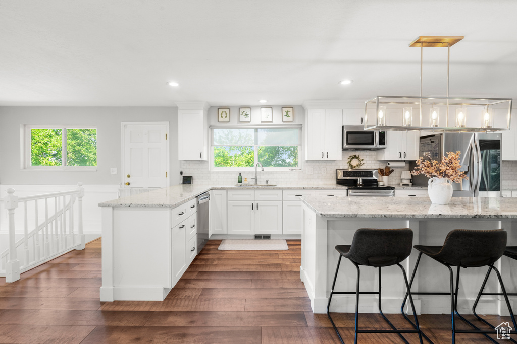 Kitchen featuring appliances with stainless steel finishes, a kitchen bar, decorative backsplash, white cabinetry, and recessed lighting