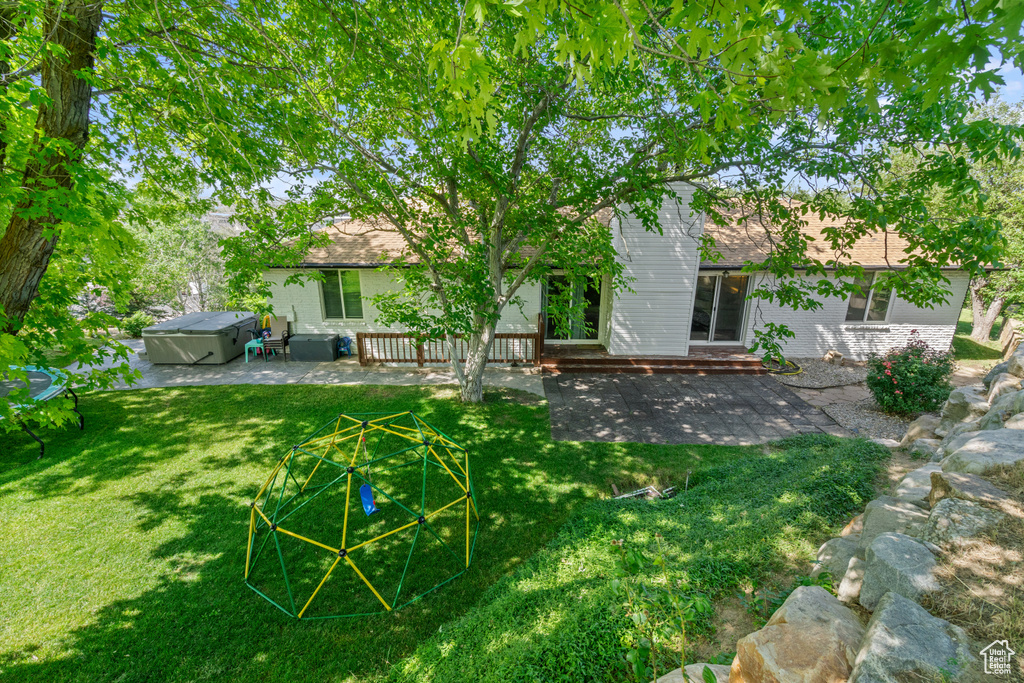 Back of house featuring a patio area, a hot tub, a lawn, and brick siding
