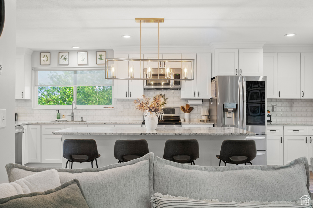 Kitchen featuring a breakfast bar, white cabinetry, decorative backsplash, stainless steel appliances, and recessed lighting