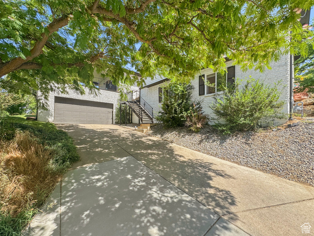 View of front facade featuring concrete driveway, brick siding, stairs, and an attached garage