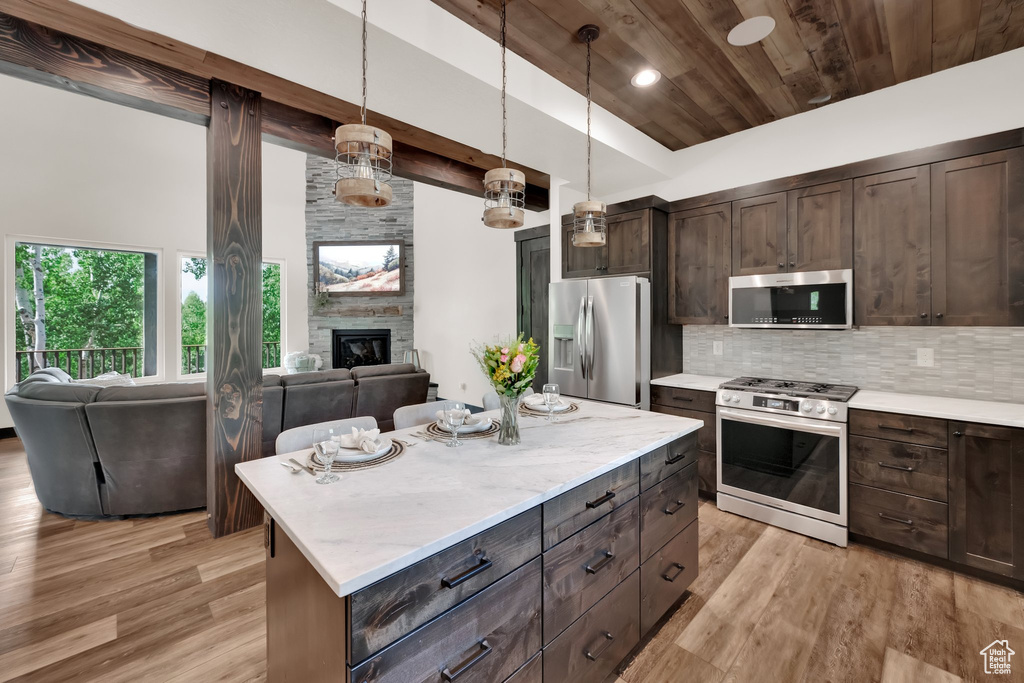 Kitchen featuring appliances with stainless steel finishes, open floor plan, wood ceiling, light wood finished floors, and a stone fireplace