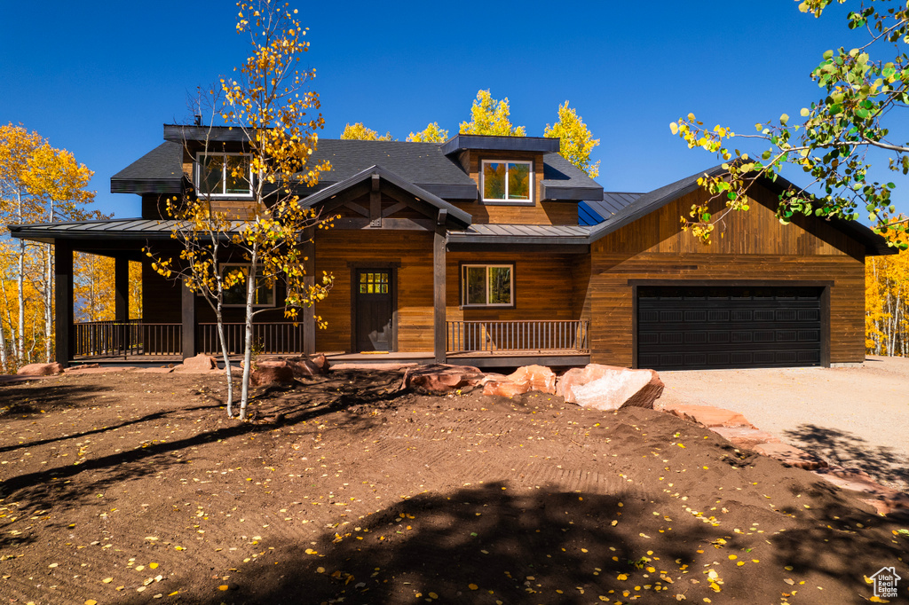 View of front facade with a porch, a standing seam roof, a metal roof, a garage, and driveway