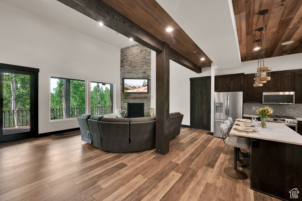 Living room with a stone fireplace, light wood-style flooring, high vaulted ceiling, a wooden ceiling with exposed beams, and recessed lighting