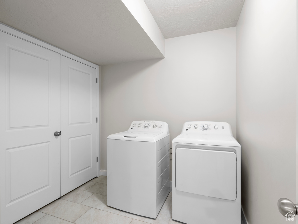 Washroom featuring independent washer and dryer, light tile patterned floors, and a textured ceiling