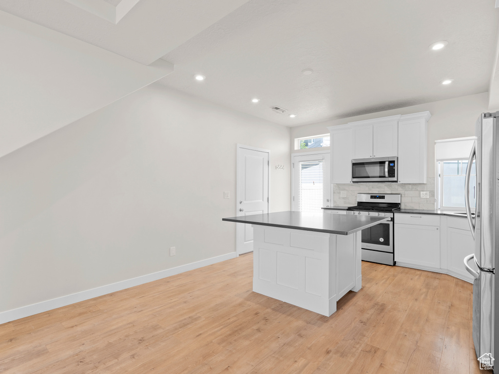 Kitchen with stainless steel appliances, dark countertops, light wood finished floors, decorative backsplash, and white cabinetry