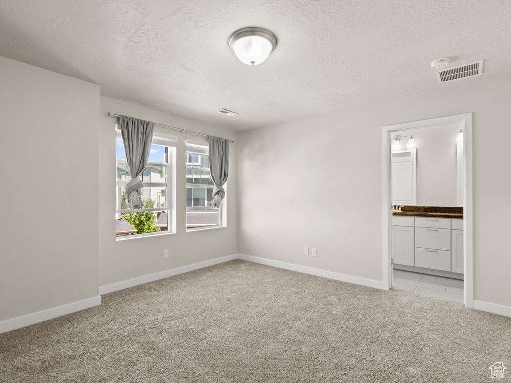 Unfurnished bedroom with a textured ceiling, light carpet, and ensuite bathroom