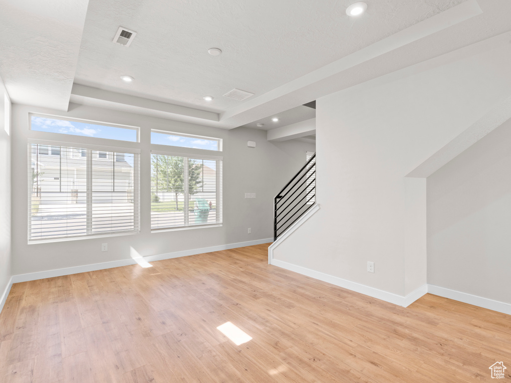 Unfurnished living room with stairs, light wood finished floors, a tray ceiling, and recessed lighting