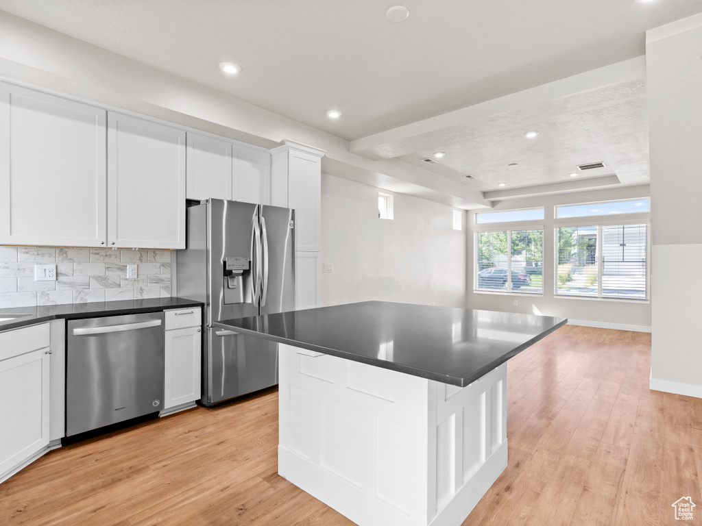 Kitchen featuring stainless steel appliances, dark countertops, light wood-style floors, decorative backsplash, and white cabinetry