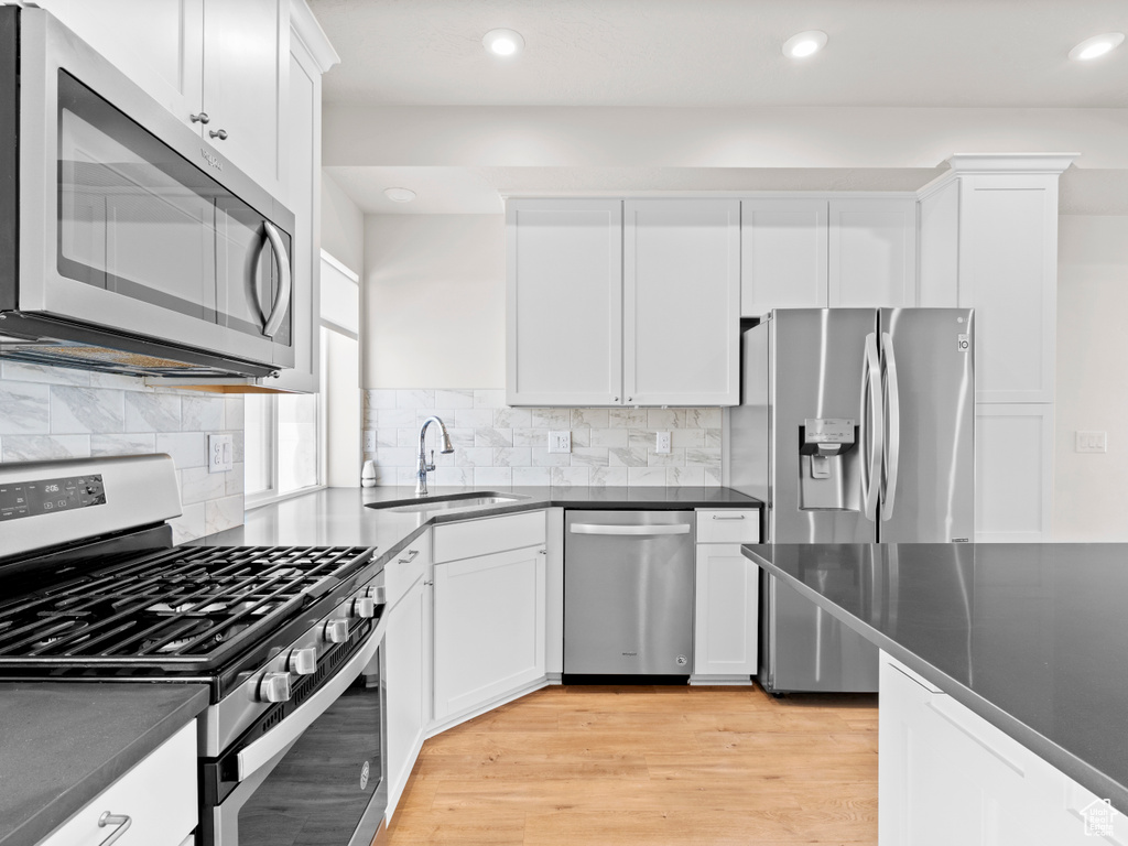 Kitchen with stainless steel appliances, dark countertops, white cabinetry, light wood finished floors, and recessed lighting