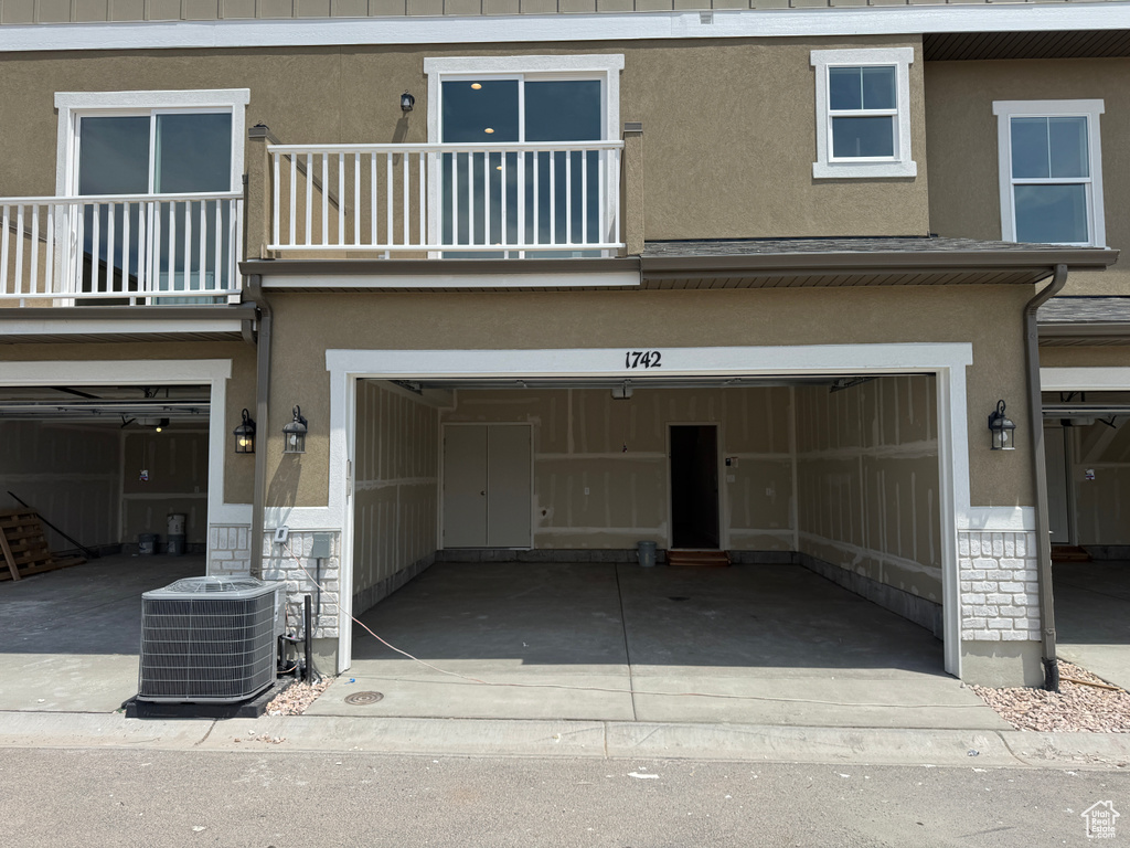 Rear view of property featuring an attached garage, a balcony, stucco siding, and driveway