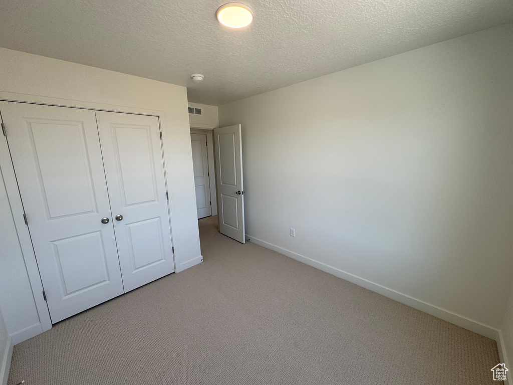 Unfurnished bedroom with light carpet, a closet, and a textured ceiling