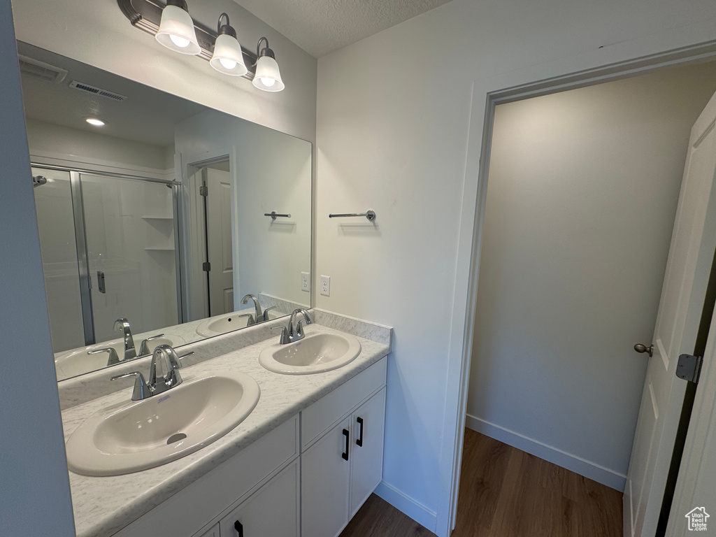 Bathroom with wood finished floors, double vanity, and a shower stall