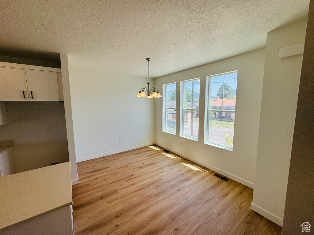Unfurnished dining area featuring light wood-type flooring, a chandelier, and a textured ceiling