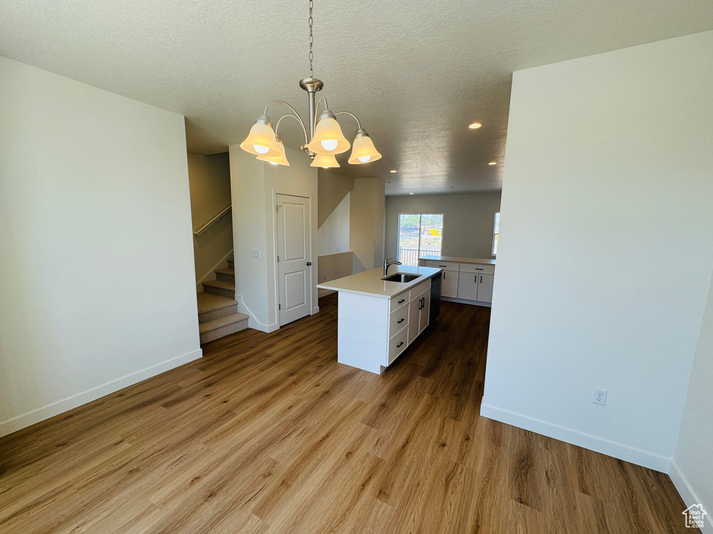 Kitchen featuring white cabinetry, light countertops, a chandelier, wood finished floors, and hanging light fixtures
