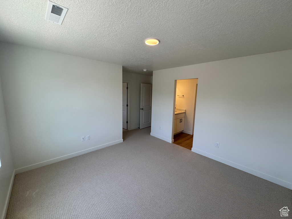 Unfurnished bedroom featuring carpet flooring, a textured ceiling, and connected bathroom