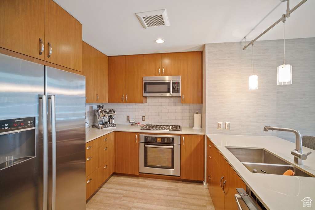 Kitchen featuring stainless steel appliances, light wood-style floors, light countertops, brown cabinetry, and recessed lighting
