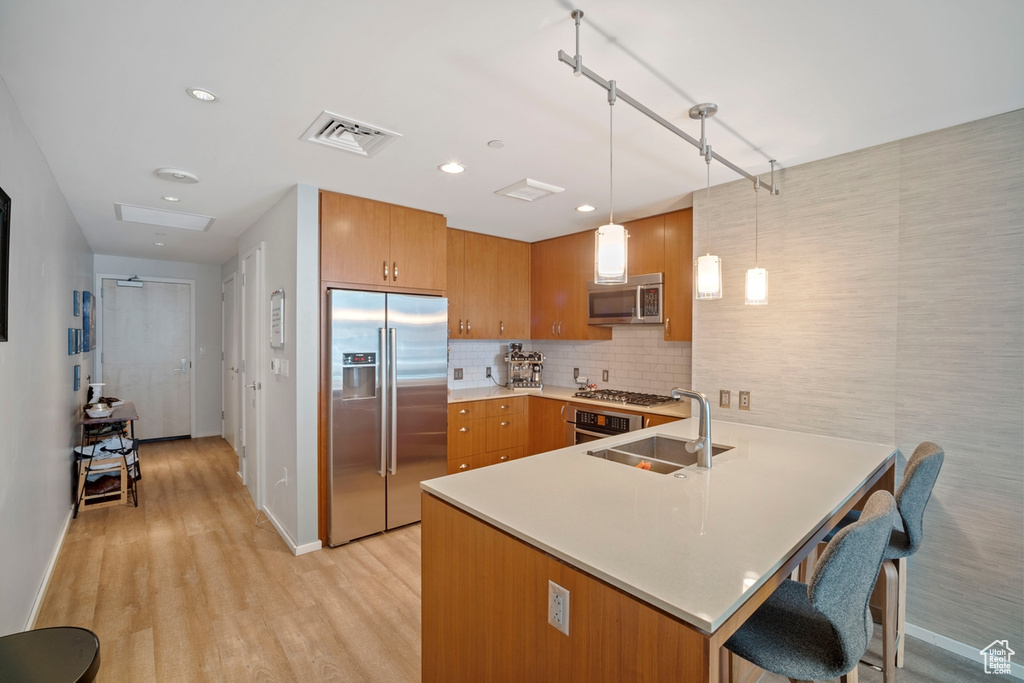 Kitchen featuring appliances with stainless steel finishes, a peninsula, brown cabinets, light countertops, and light wood-style floors