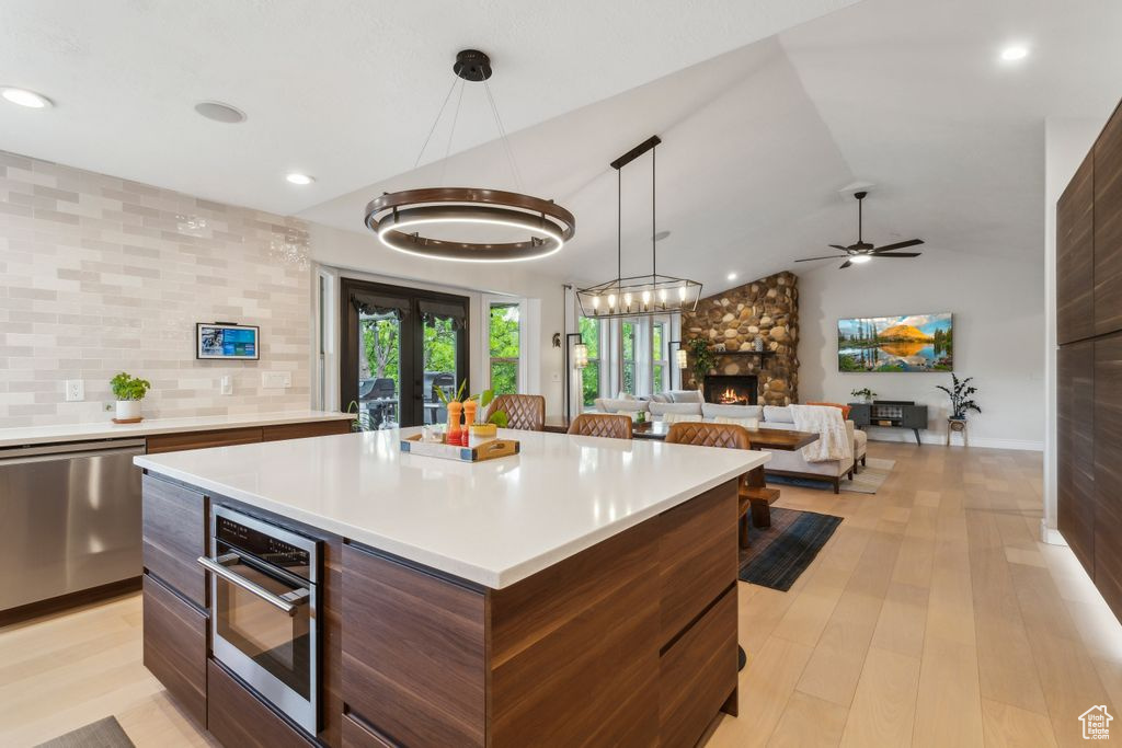 Kitchen featuring modern cabinets, stainless steel appliances, a stone fireplace, light countertops, and ceiling fan