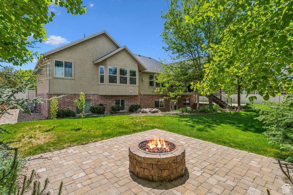 Rear view of property featuring an outdoor fire pit, stucco siding, a patio, and a yard