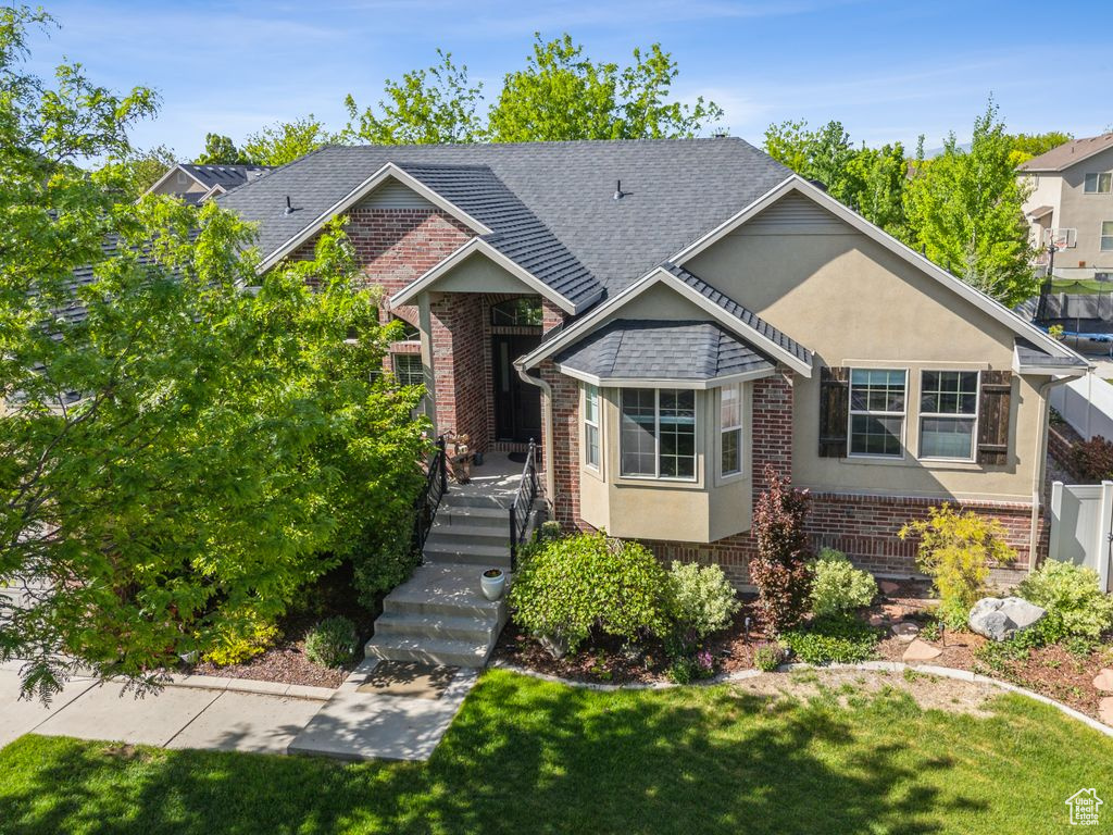 Bungalow featuring brick siding, a shingled roof, a front lawn, and stucco siding
