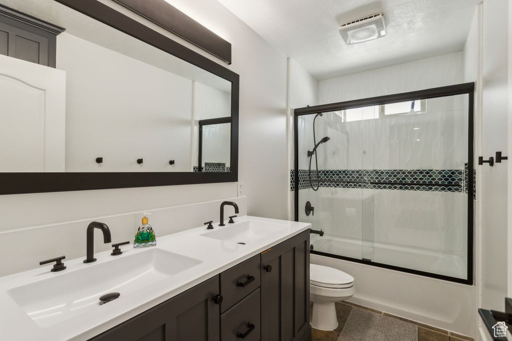 Bathroom featuring double vanity, shower / bath combination with glass door, and tile patterned floors